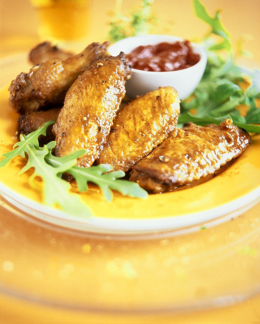 Chicken wings with salsa dip and rocket on yellow plate