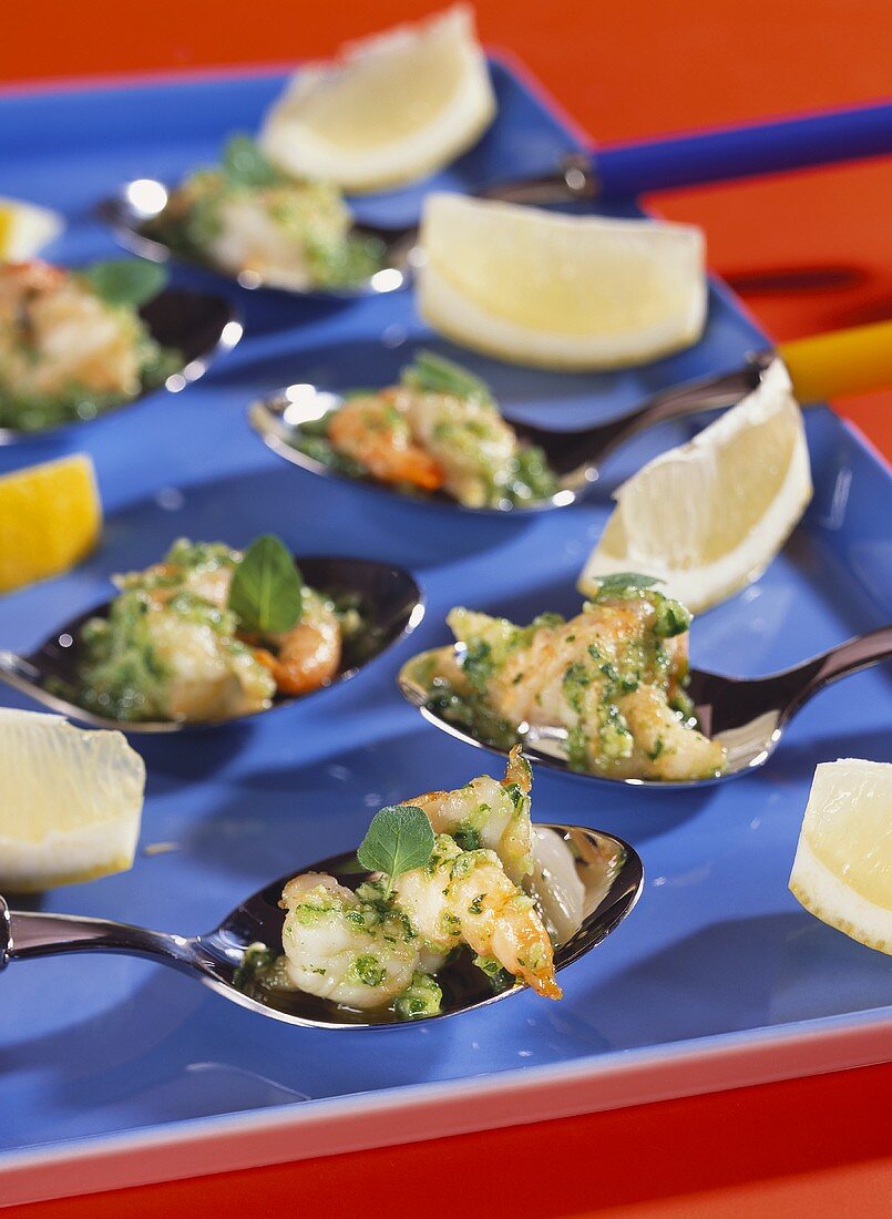 Shrimps with oregano on spoons; lemon wedges