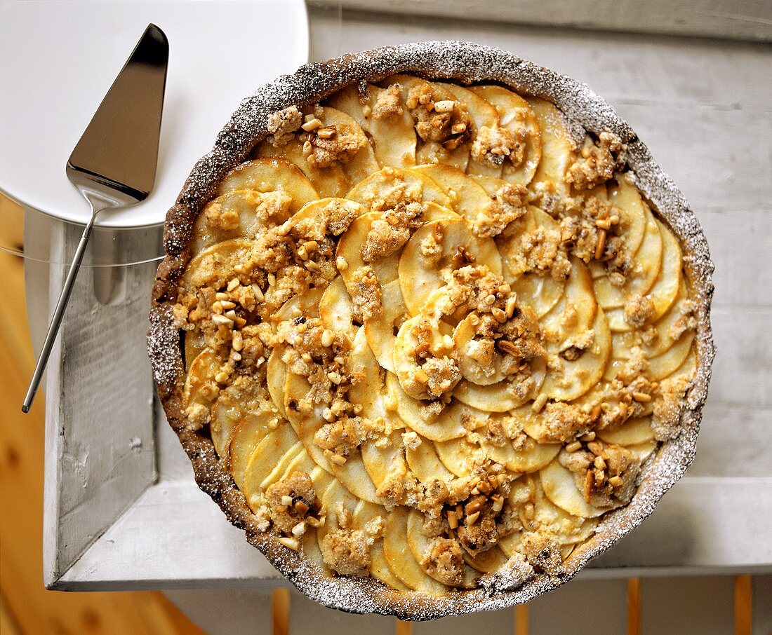 Whole apple tart with crumble and pine nuts on tray