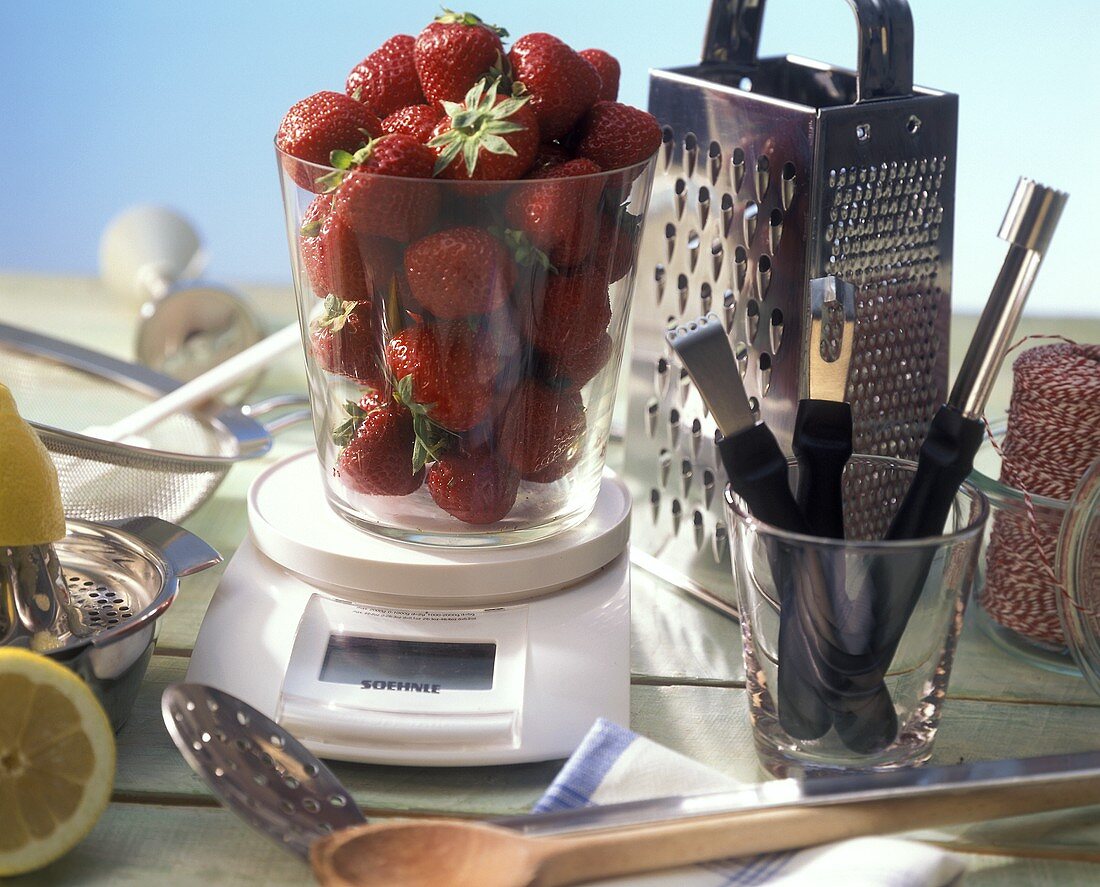 Erdbeeren auf Waage, umgeben von Küchenwerkzeugen