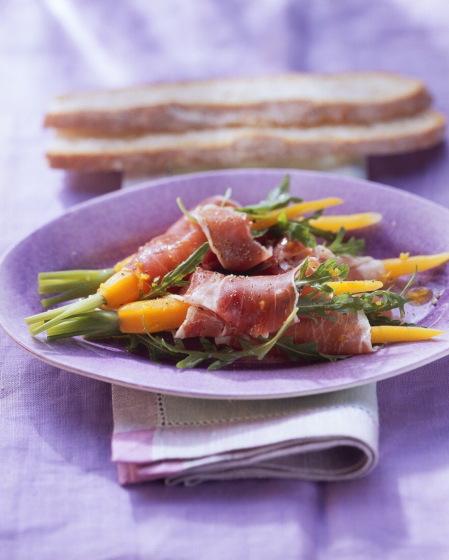 Rucola-Schinken-Möhrchen auf lila Platte; Brotscheiben