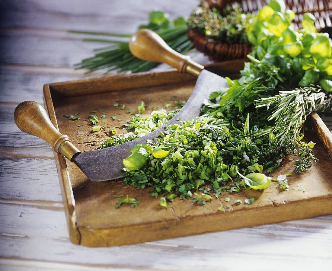 Chopped herbs with mezzaluna on wooden chopping board