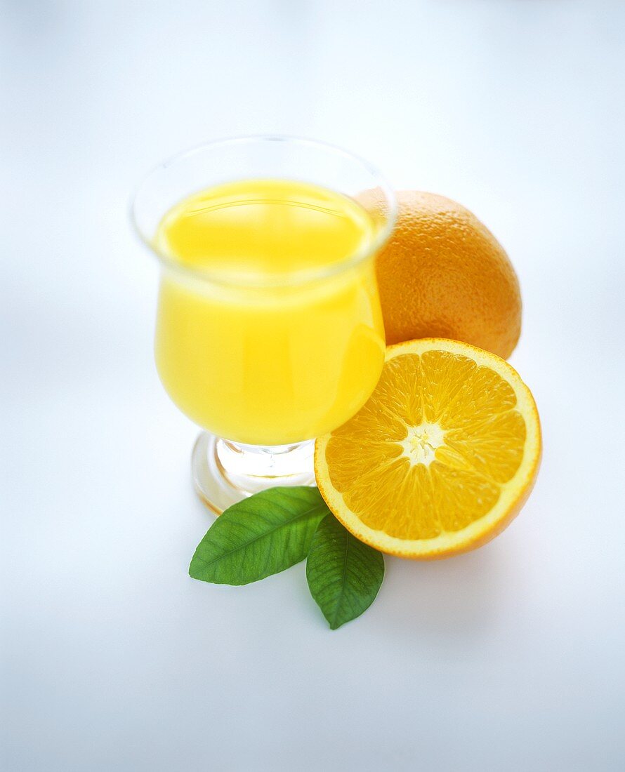 Orange juice in glass beside fresh oranges
