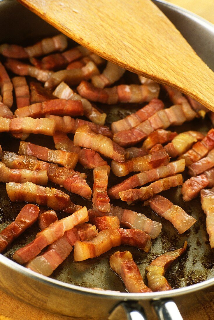 Frying strips of bacon in frying pan