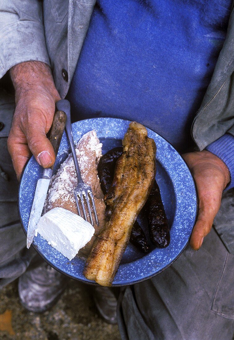 Korsischer Bauer hält Teller mit Fleisch, Polenta und Käse