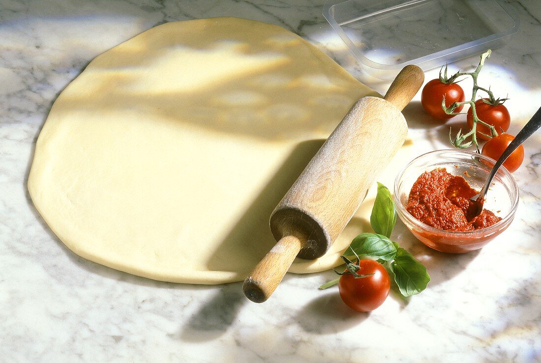 Ausgerollter Pizzateig, Tomatensauce und frische Tomaten