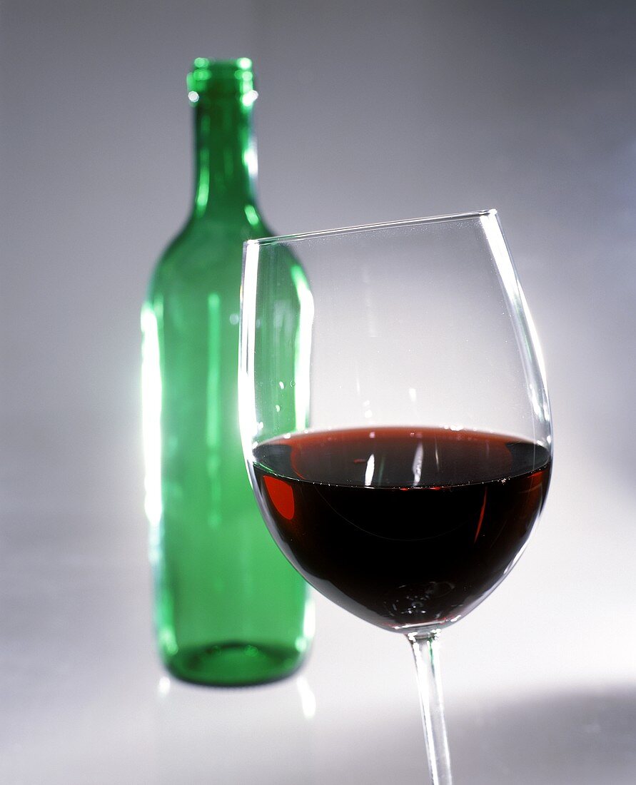 Red wine in glass in front of green bottle