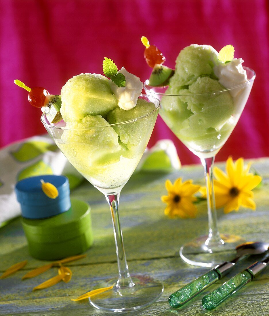 Kiwi fruit sorbet in glasses with cream and skewered fruit
