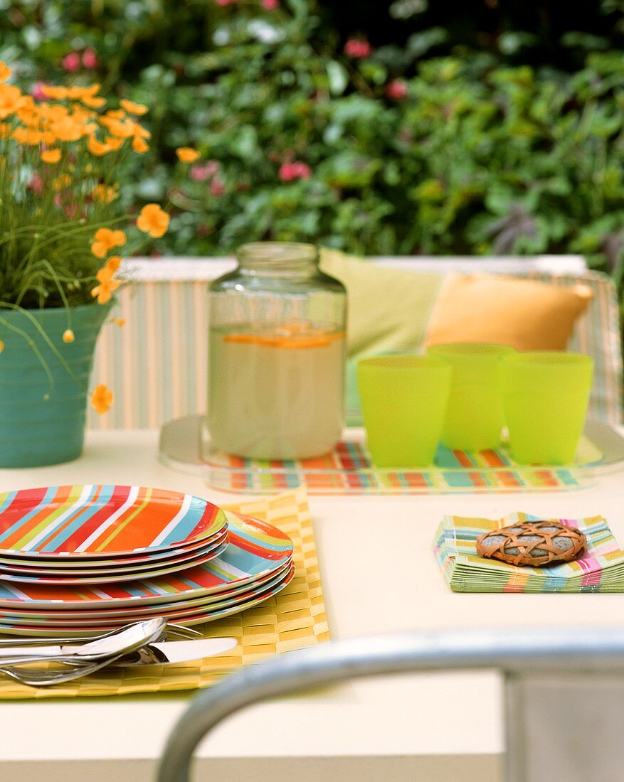 Sommerlicher Tisch im Garten mit bunten Tellern und Limonade
