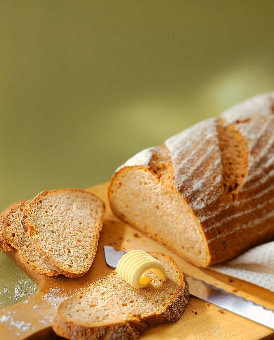 Landbrot mit abgeschnittenen Scheiben und Butterröllchen