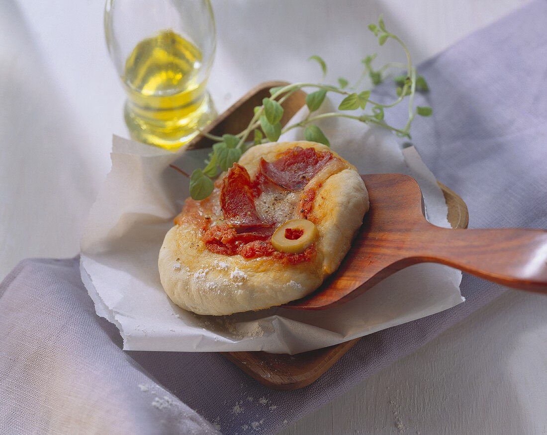 Salami mini-pizza with olives on baking paddle