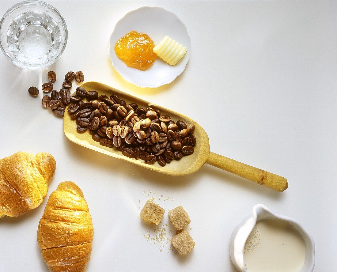Kaffeebohnen auf Schaufel, Croissants, Butter, Marmelade etc.
