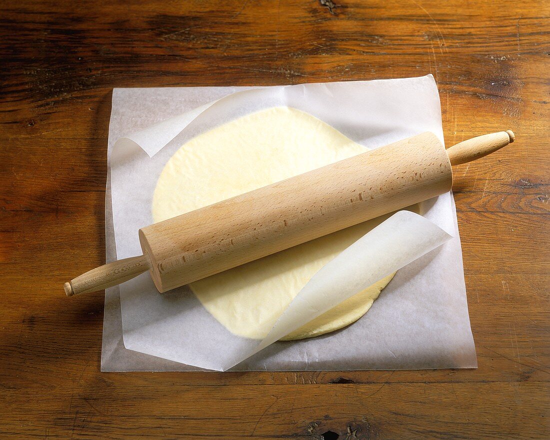 Pastry rolled out between  baking paper with rolling pin