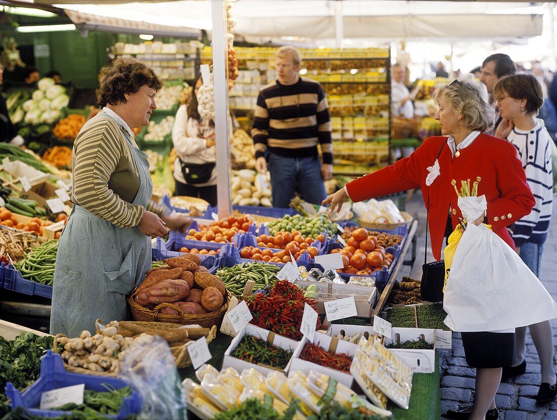 Woman at market stall pointing to vegetables