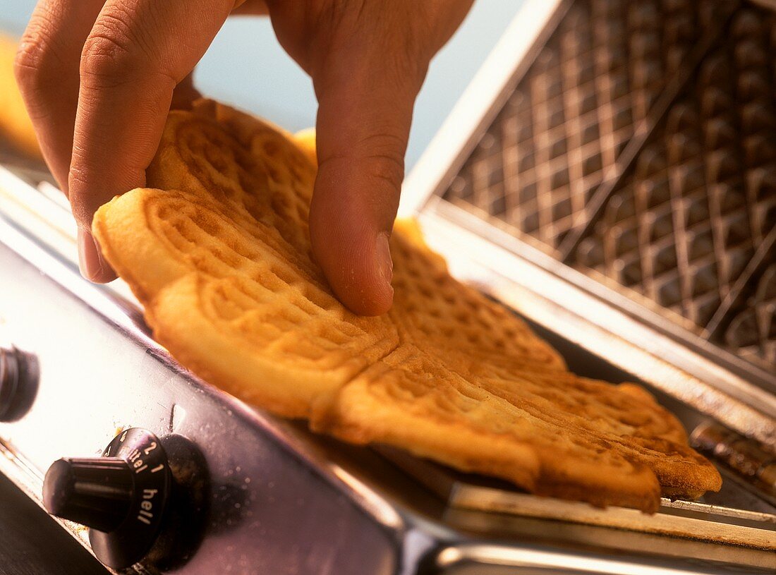 Hand taking freshly baked waffle out of waffle iron