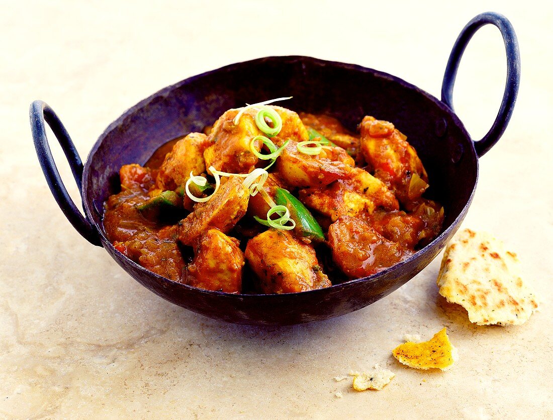 Chicken with spicy sauce in cast-iron pan; flatbread