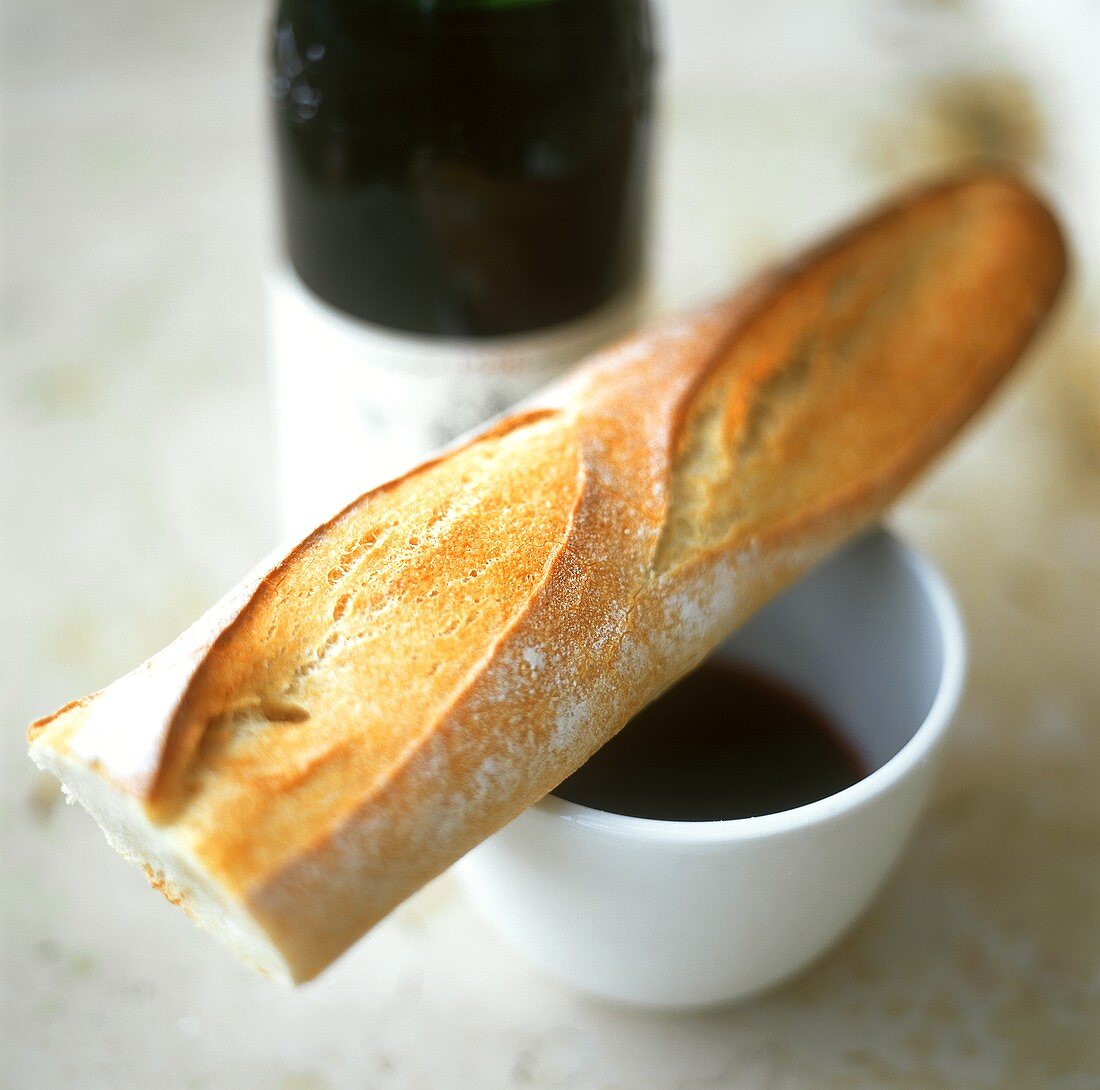 Baguette on coffee cup in front of red wine bottle