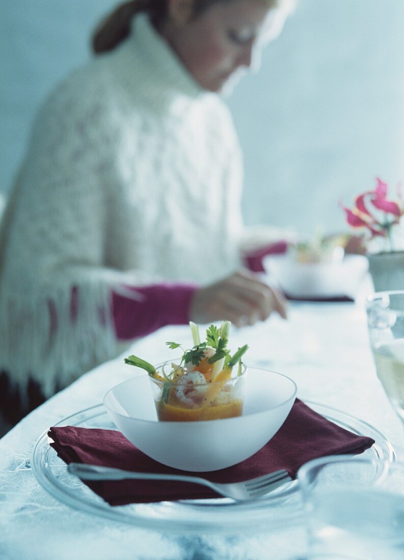 Shrimps-Möhren-Cocktail auf Tisch; Frau im Hintergrund