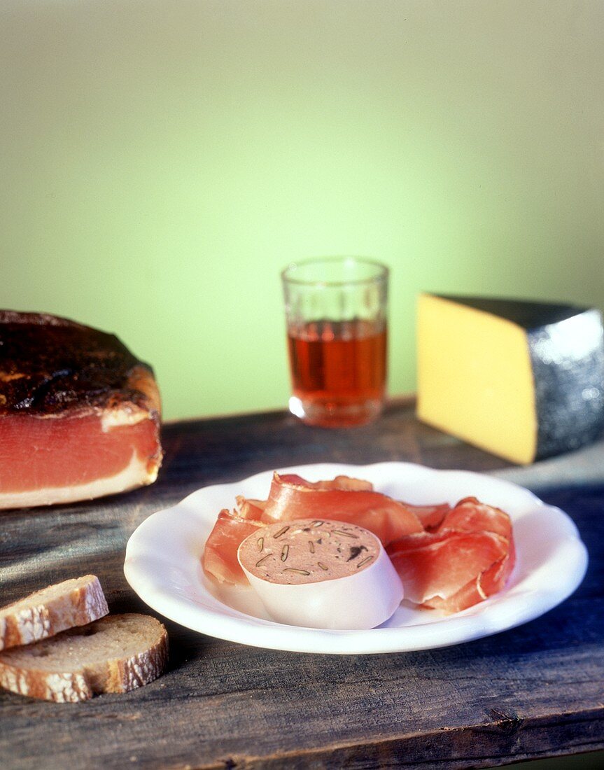 Speck, Leberwurst, Käse, Rotwein und Brot auf Holzplatte