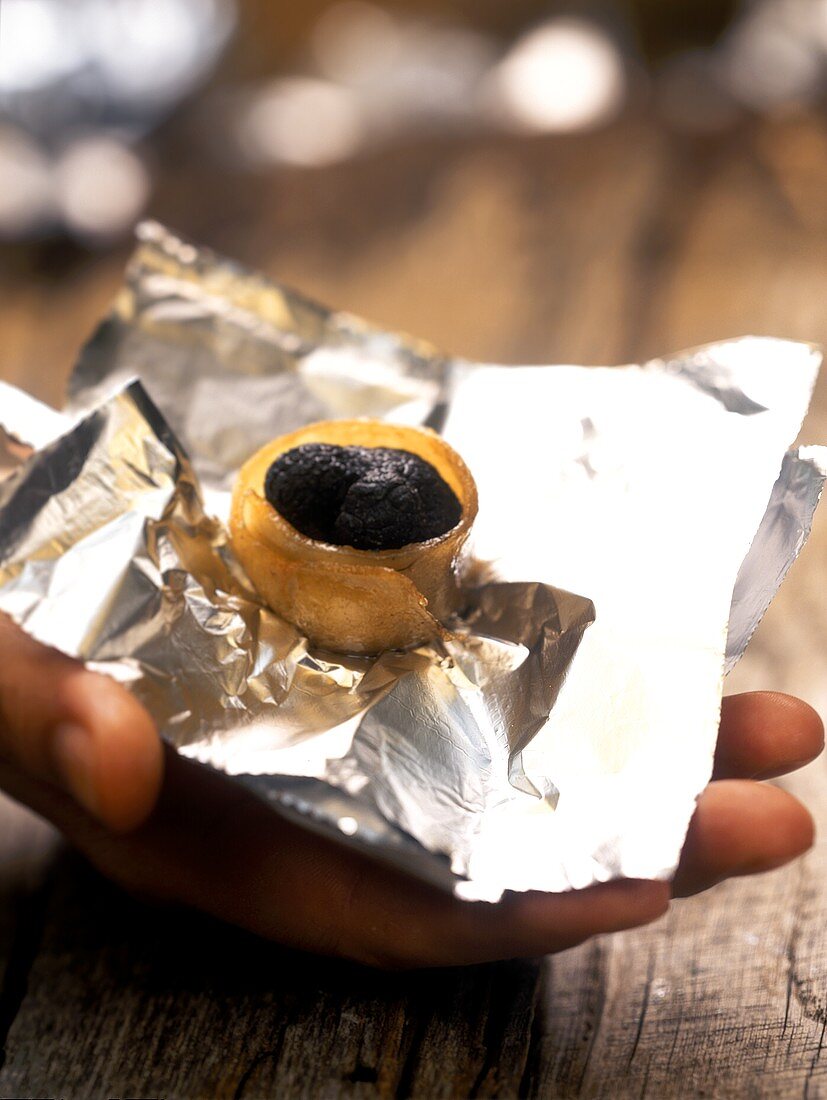 Hand holding truffle roasted in bacon on aluminium foil