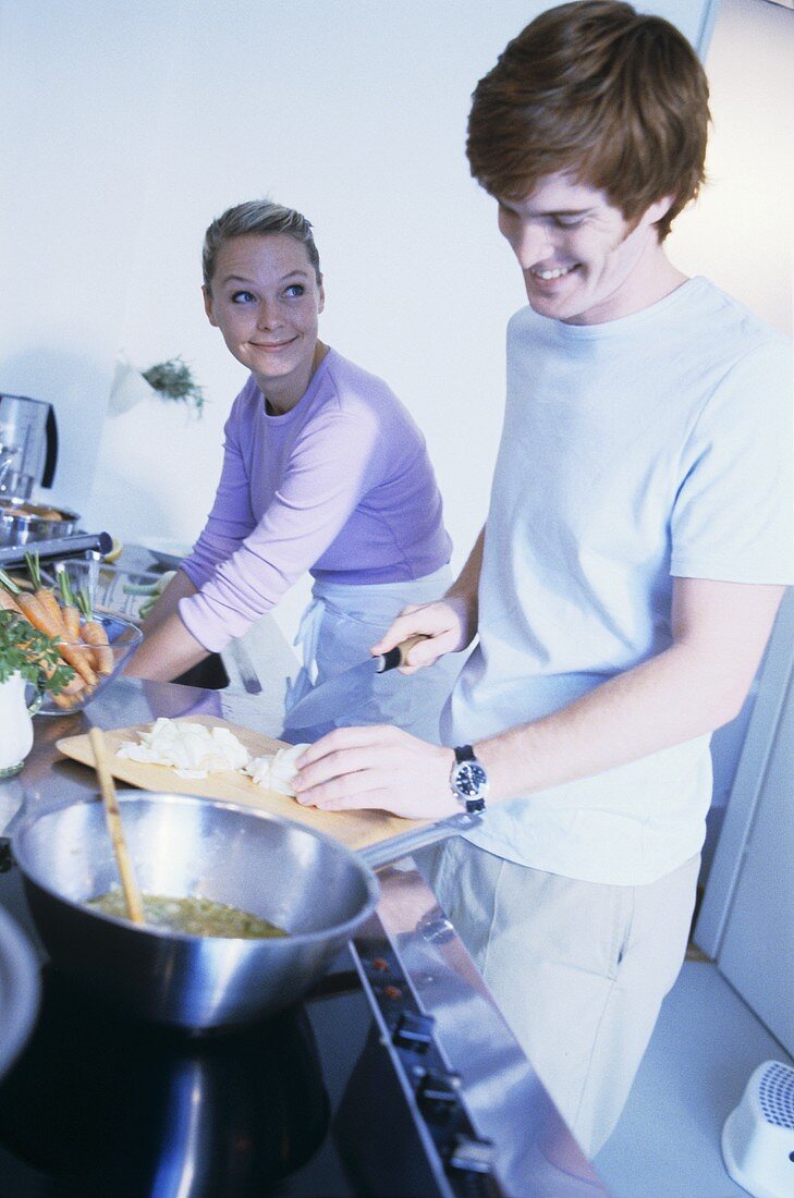Young couple in kitchen cutting onions and washing up