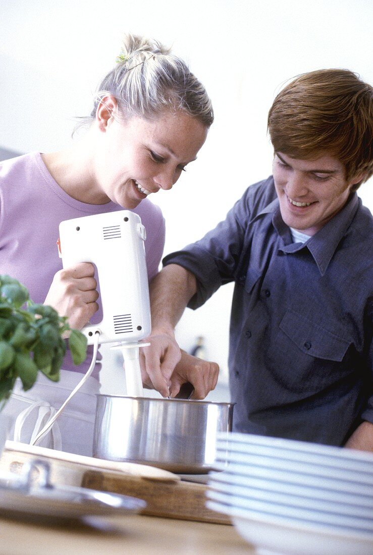 Young couple stirring contents of pan with mixer