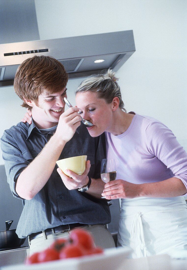 Young couple in the kitchen tasting soup from spoon