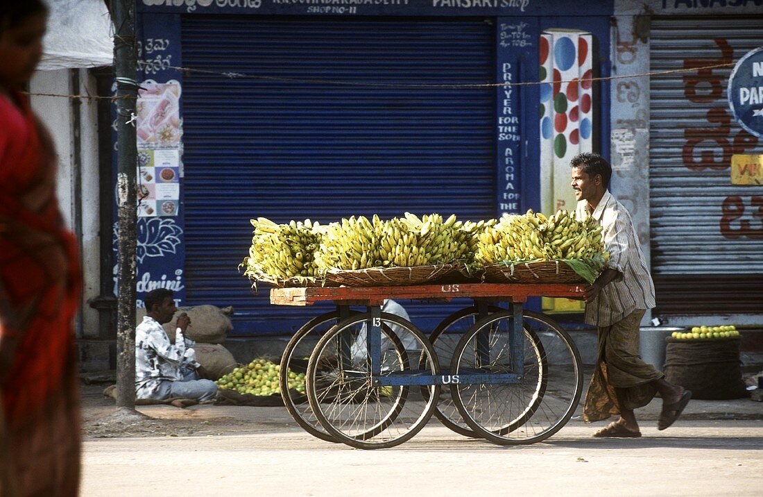 Indischer Marktverkäufer schiebt Karren mit Bananen
