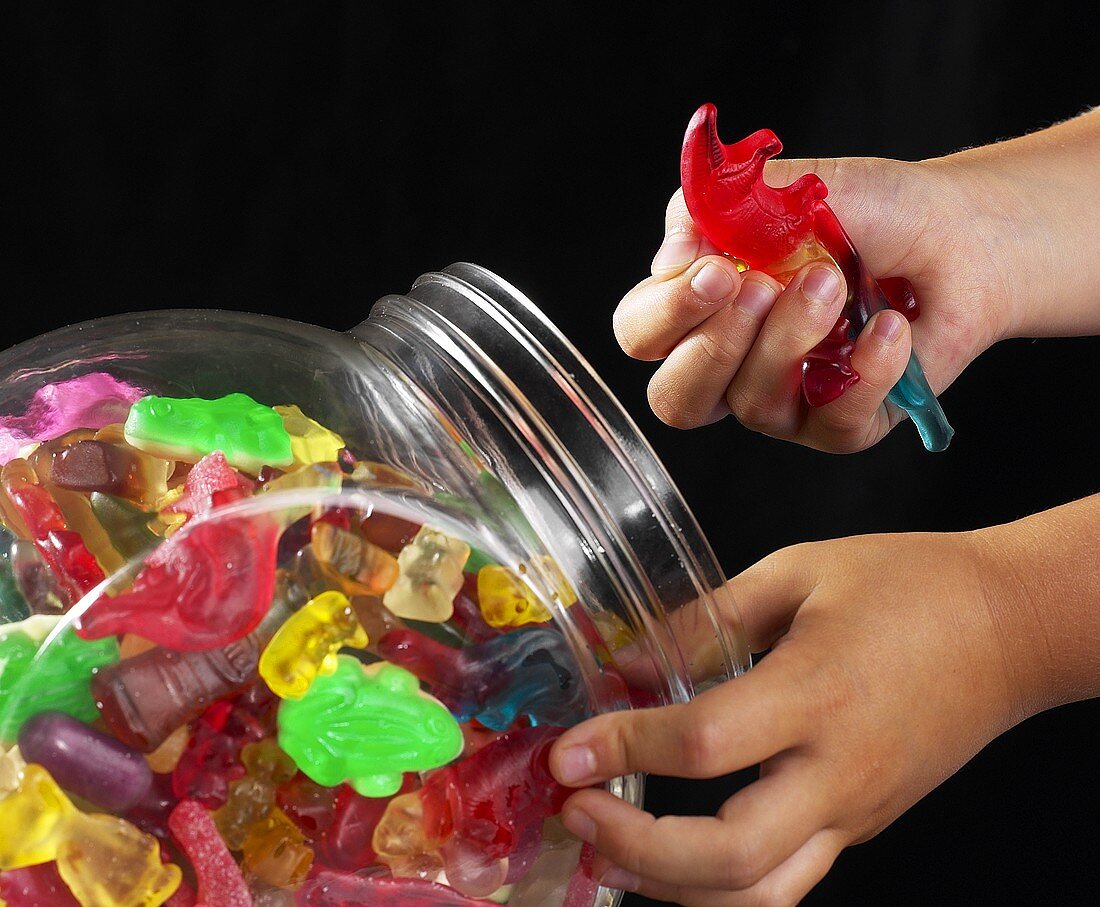 Kinderhände holen bunten Fruchtgummi aus Glasbehälter