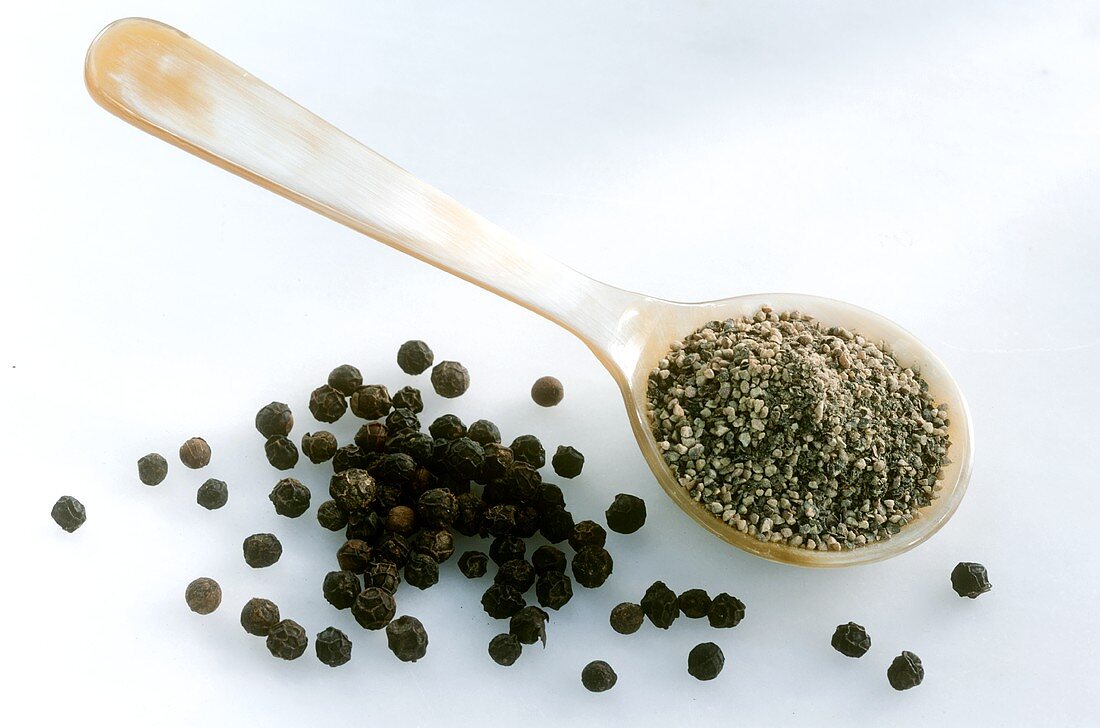 Ground pepper on spoon and black peppercorns