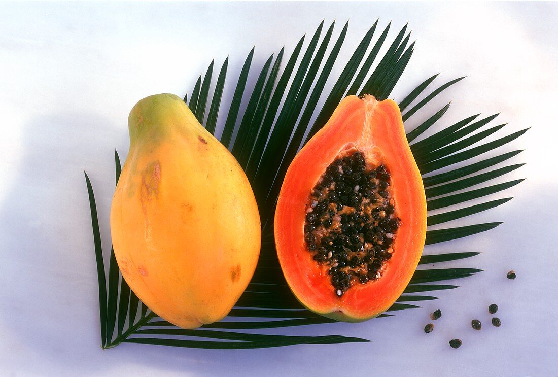 Whole and half papaya on palm leaf