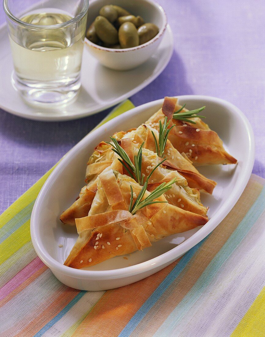 Käse-Kräuter-Ecken mit Sesam; Oliven; Wein (Griechenland)