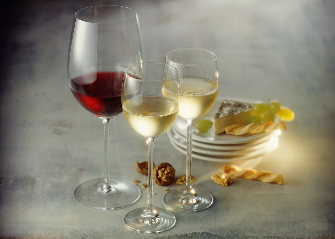 Rotweinglas und zwei Weissweingläser; Käse; Käsegebäck; Nüsse