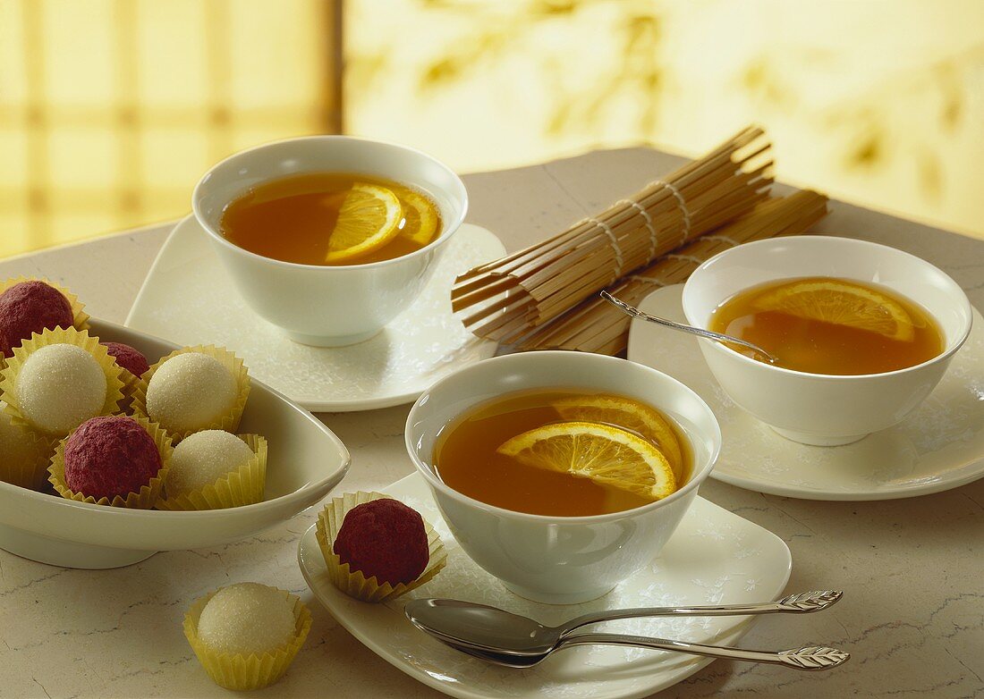 Drei Tassen Tee mit Orangenscheiben; Trüffelpralinen