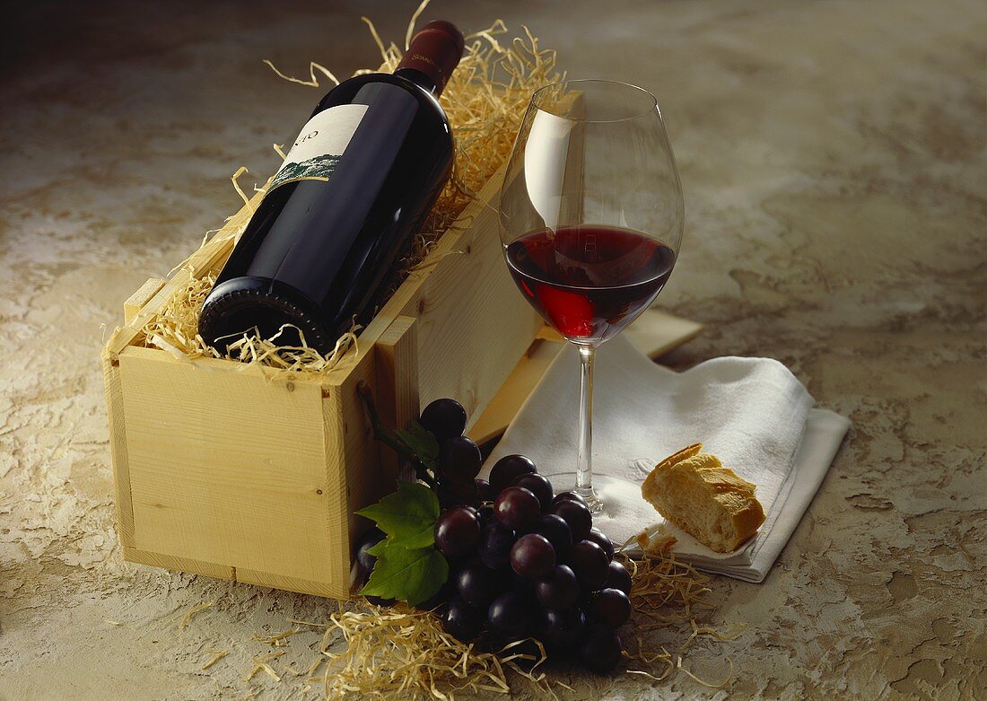 Red wine bottle in wooden crate; red wine glass; red grapes