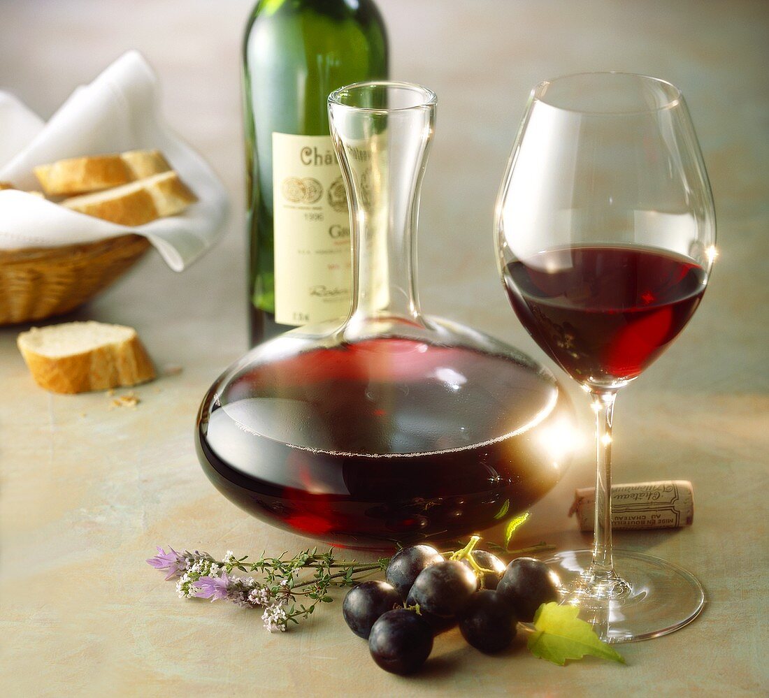 Rotwein in Glas, Karaffe und Flasche; rote Trauben; Baguette