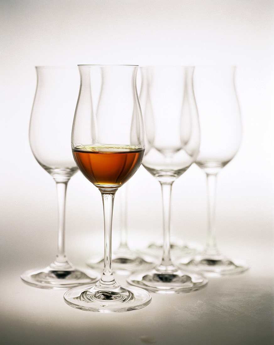 Glass of cognac in front of empty cognac glasses