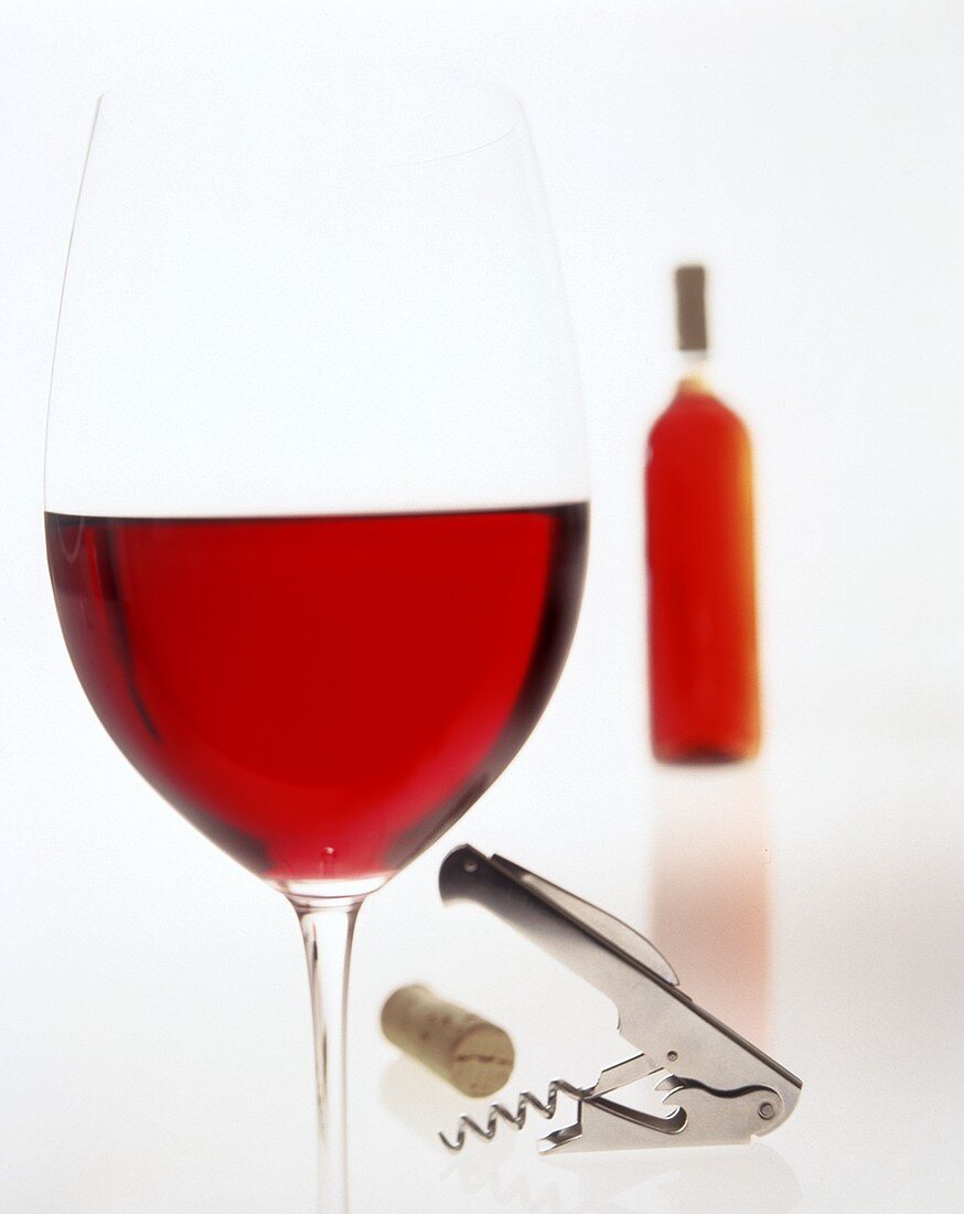 Glass of red wine in front of bottle; cork; corkscrew