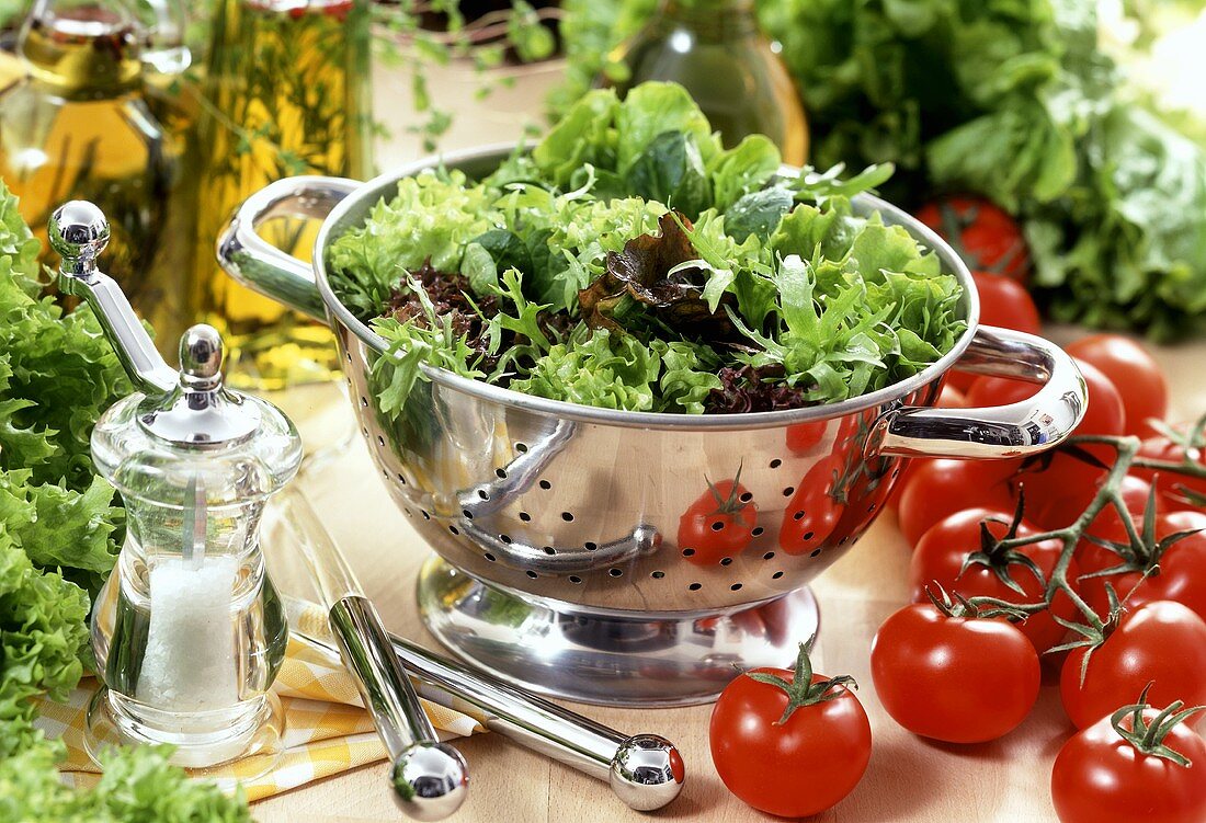 Mixed salad in strainer; tomatoes; salt; oil