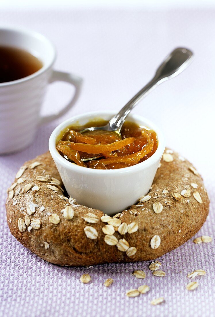Orange marmalade in bowl on oat bread; tea
