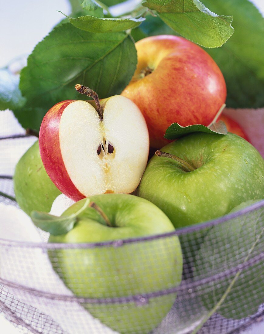 Green and red apples with leaves in wire basket