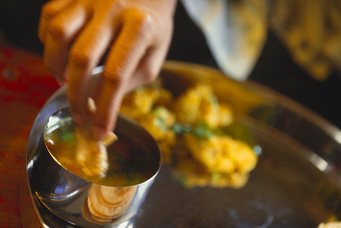 Hand taucht Stück Brot in indisches Curry