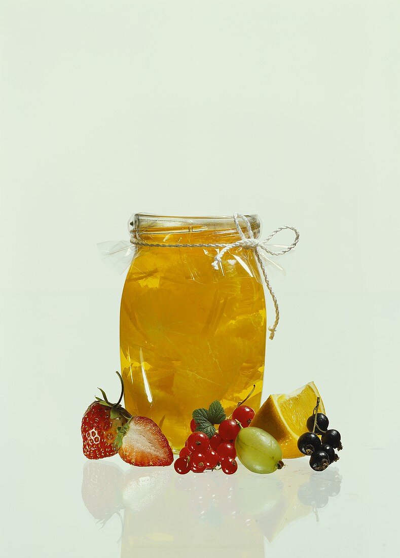 Orange jelly in glass, surrounded by berries & orange slice