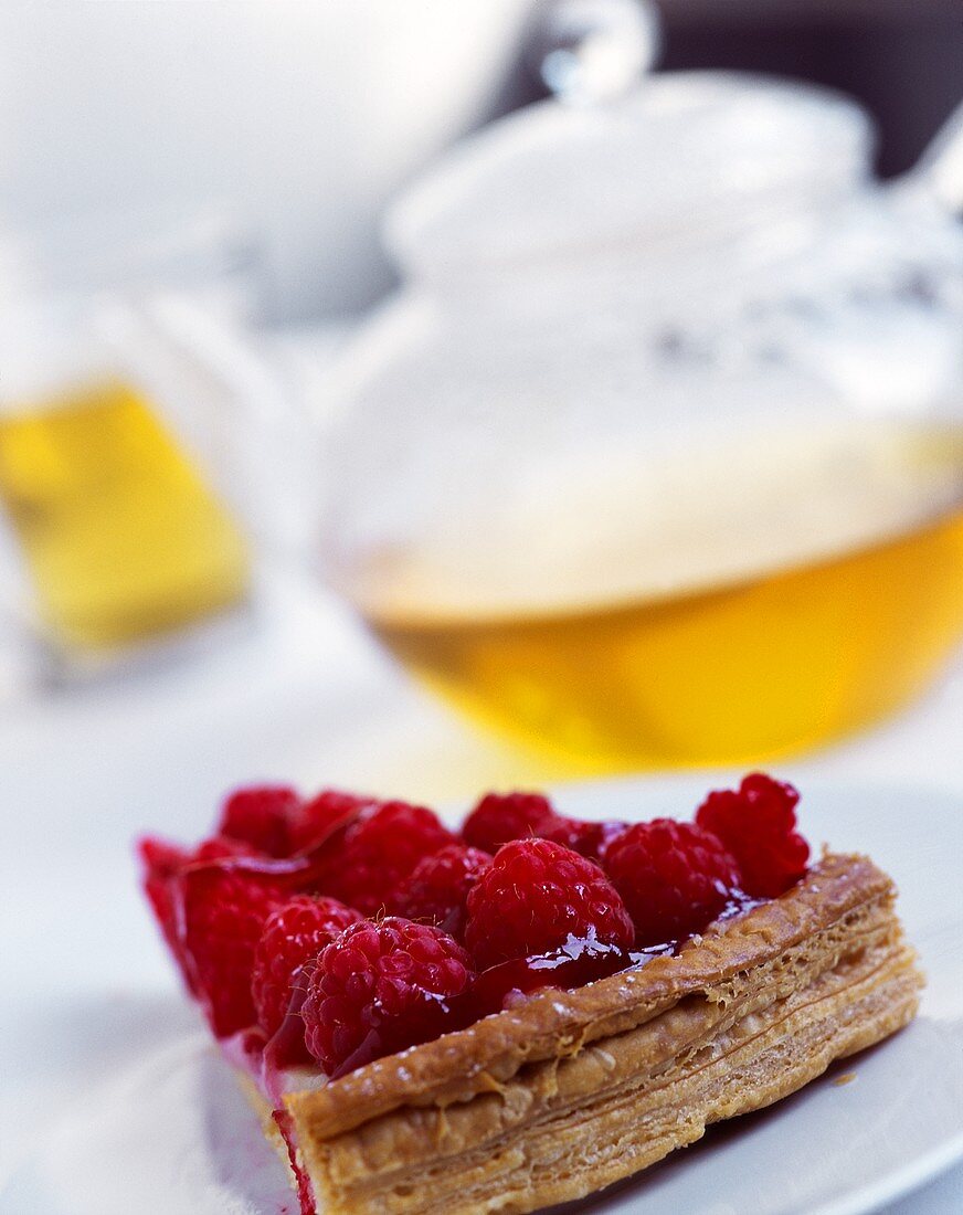 Piece of raspberry flan in front of teapot