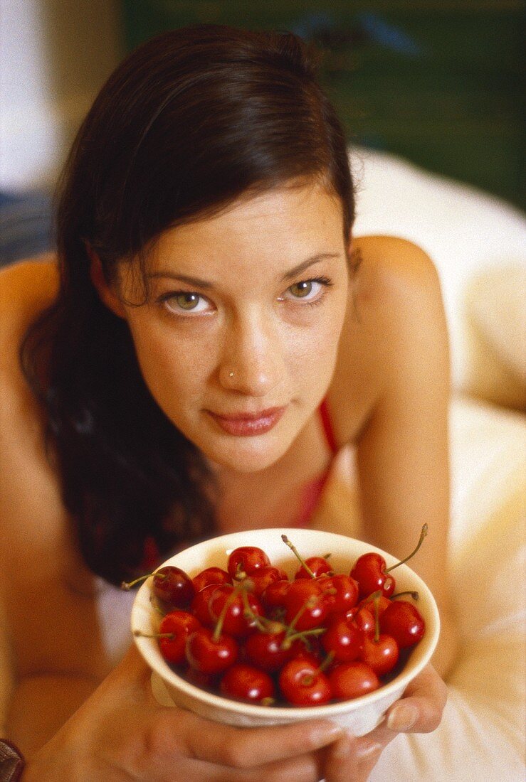 Young woman holding bowl of fresh cherries