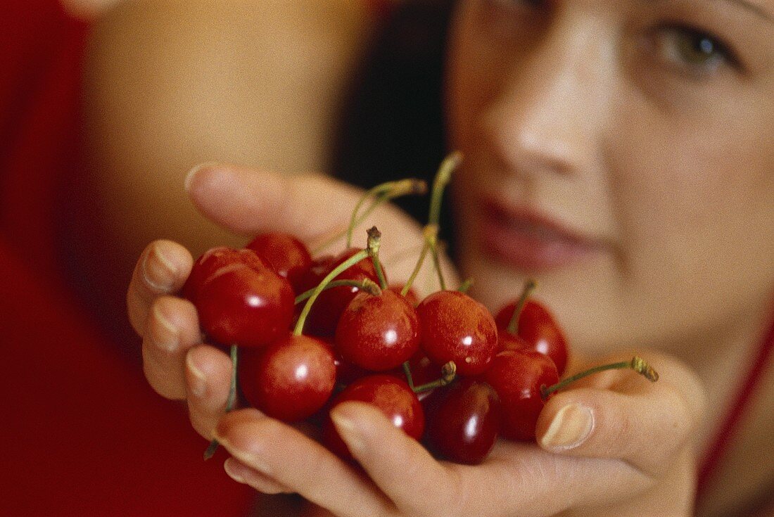 Young woman holding red cherries in both hands