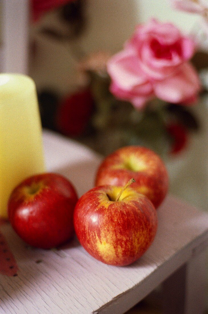 Drei frische Äpfel auf Tisch; rosa Rose