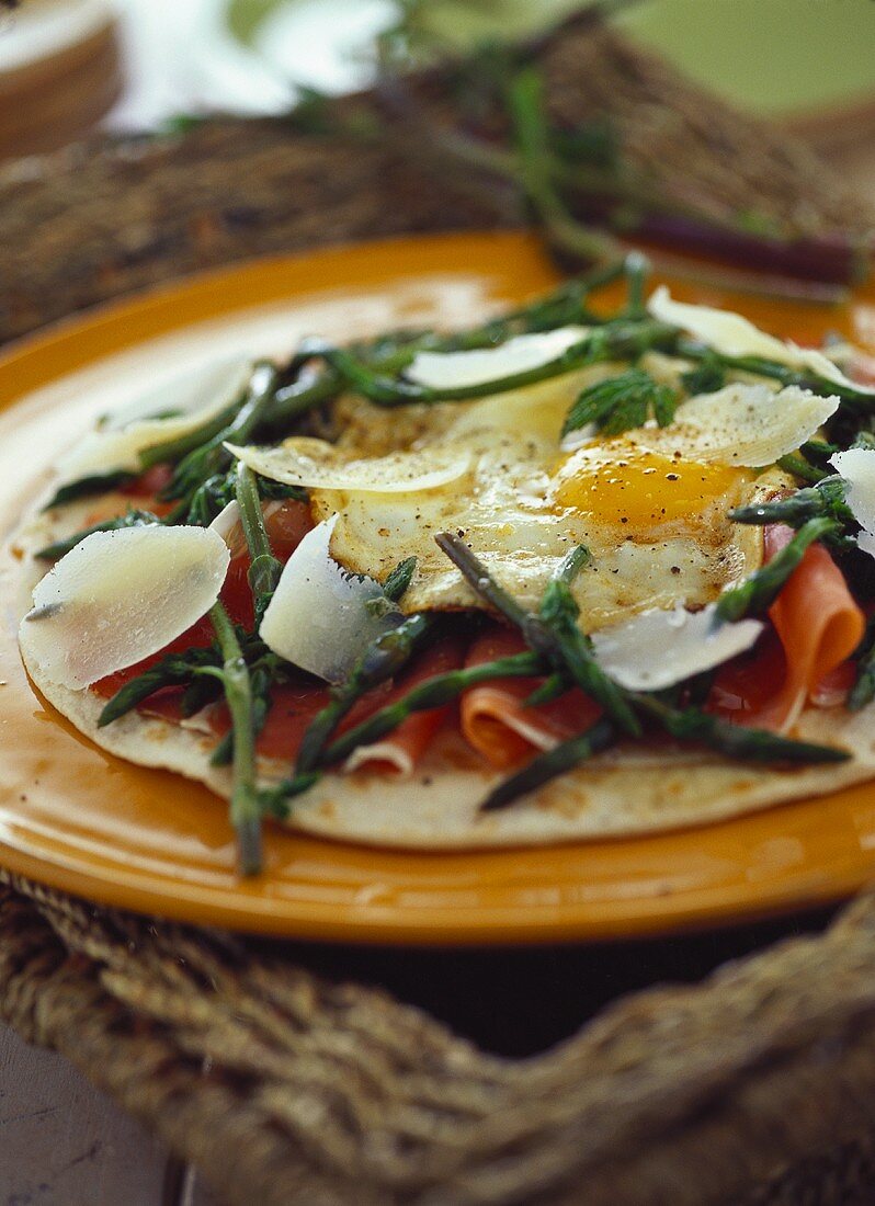 Pizza base with raw ham, fried egg and green asparagus