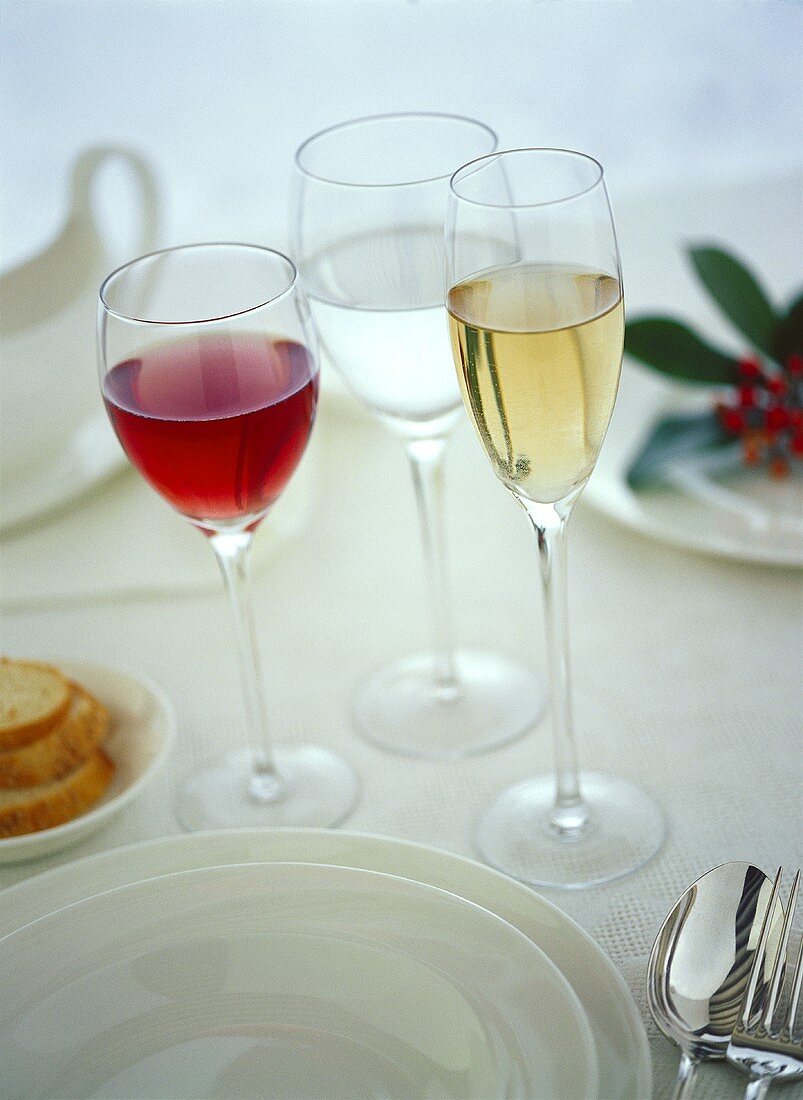 Rotweinglas, Weissweinglas und Glas Wasser neben Gedeck