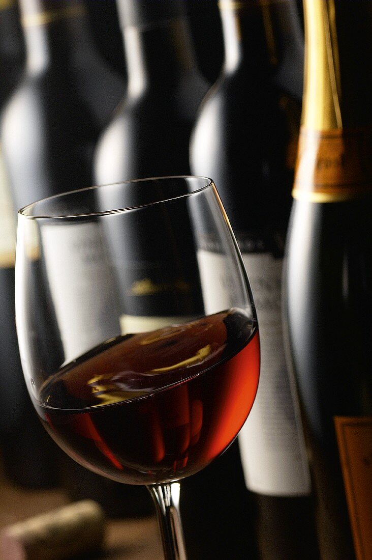 Glas Rotwein vor Weinflaschen